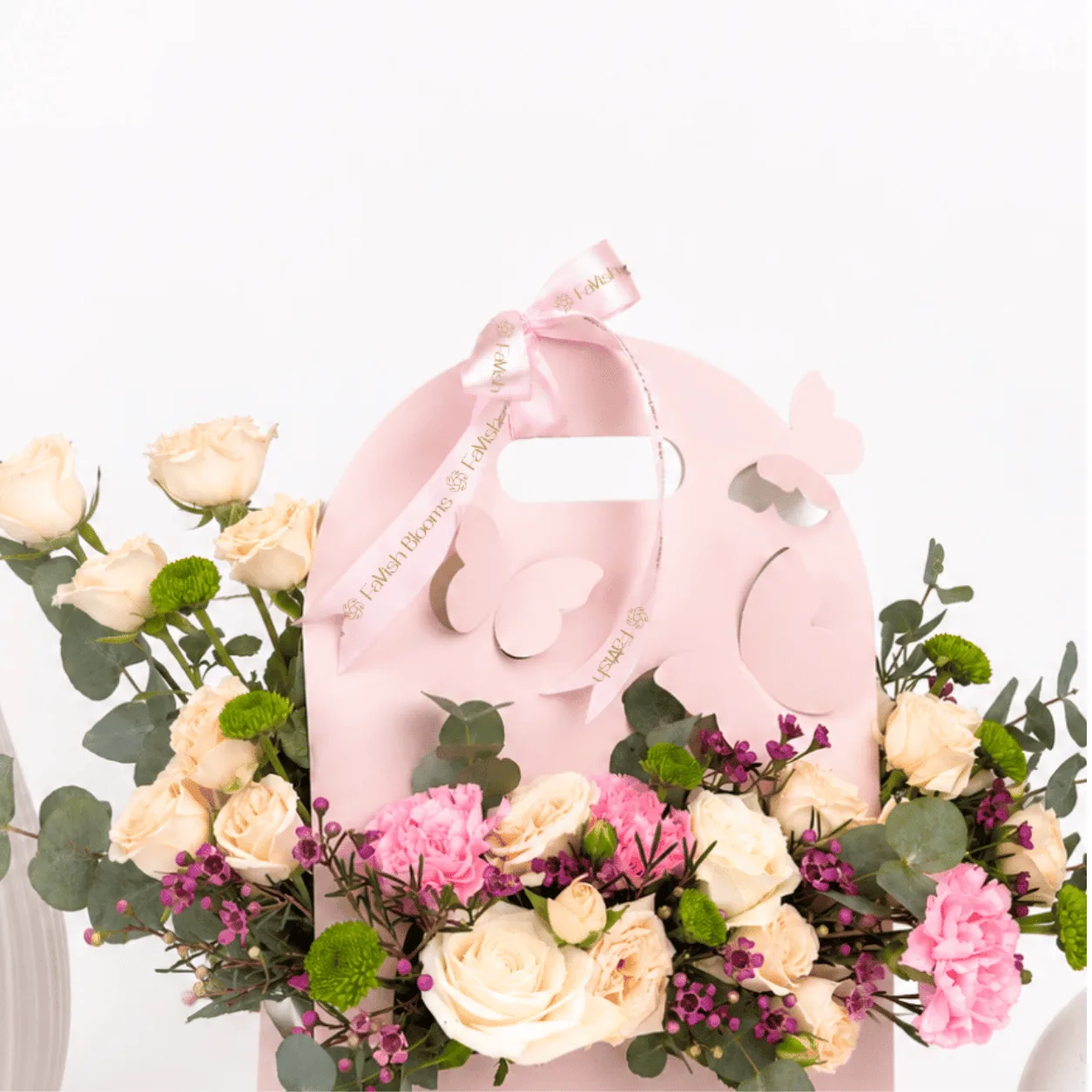 Close-up of a pastel floral arrangement in a pink Favish Blooms gift bag featuring cream roses, pink carnations, spray roses, eucalyptus, and seasonal blooms.
