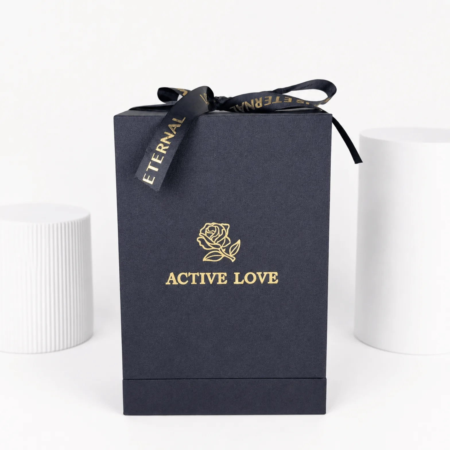 Premium black luxury gift box with gold logo and satin ribbon, displayed on a clean white studio background with modern pedestal props.